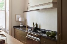 a classic rich brown kitchen with a kitchen island, a large hood and black countertops plus a vintage cooker