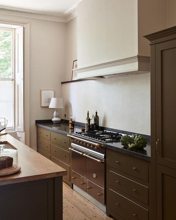 a classic rich brown kitchen with a kitchen island, a large hood and black countertops plus a vintage cooker