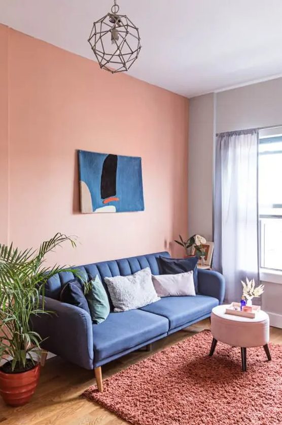 a colorful living room with a Peach Fuzz accent wall, a navy sofa, a white pouf, a pink rug and some bold artwork