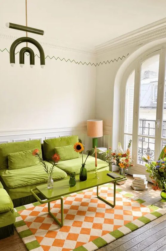 a colorful living room with a chartreuse sectional, a matching coffee table, a printed rug and blooms around
