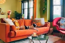 a colorful living room with chartreuse walls, an orange sofa and a pink chair, some plants and pendant lamps