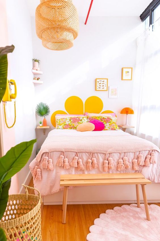 a colorful modern teen bedroom with a bed and pink and yellow bedding, a bench, a basket and artwork