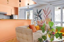 a colorful space with a Peach Fuzz kitchen and a kitchen island that separates the space, a neutral sofa, a printed rug and some plants