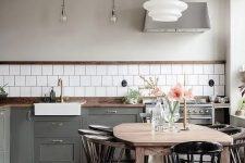 a contemporary Scandi kitchen with a white tile backsplash, dark-stained countertops, a herringbone wooden floor, a light-stained table, dark-stained chairs and a black chair