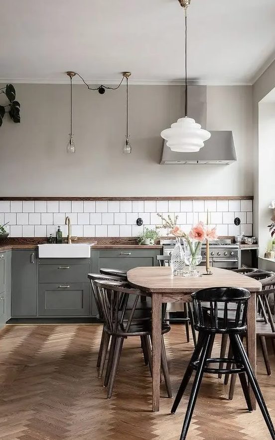 A contemporary Scandi kitchen with a white tile backsplash, dark stained countertops, a herringbone wooden floor, a light stained table, dark stained chairs and a black chair