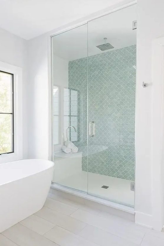a contemporary coastal bathroom with an aqua fishscale wall, all-neutrals around and a free-standing tub by the window