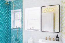 a contrasting bathroom with blue fishscale and white subway tiles, a free-standing sink, a mirror and gold fixtures