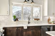 a contrasting kitchen with white and dark-stained shaker style cabinets, white stone countertops and a white mother-of-pearl chevron backsplash
