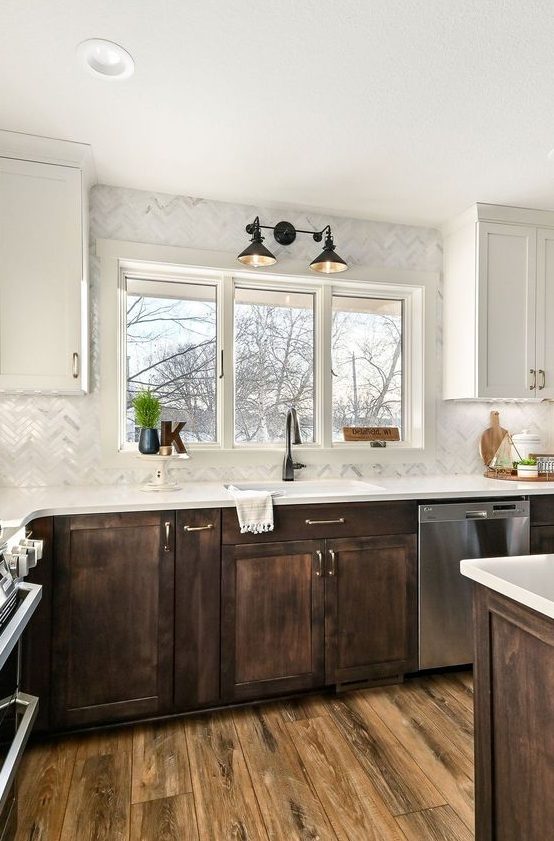 A contrasting kitchen with white and dark stained shaker style cabinets, white stone countertops and a white mother of pearl chevron backsplash