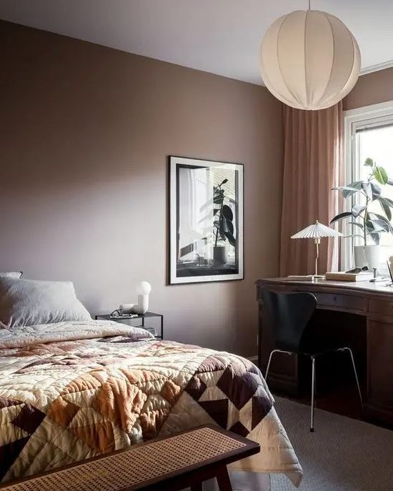 a cozy bedroom with a brown accent wall, a bed with printed bedding, a dark-stained desk, a black chair and some plants