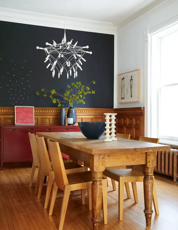 a cozy dining room with a soot accent wall, stained panels, a red credenza, a vintage dining table and chairs, a creative chandelier