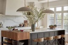 a cozy earthy kitchen with white cabinets and a black kitchen island, a small console table, tall stools and pendant lamps