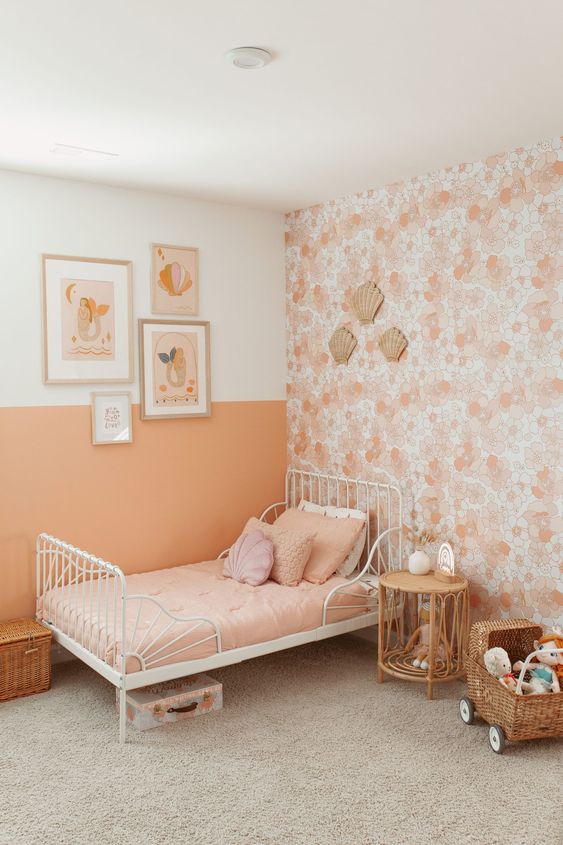 a cozy kid's room with a Peach Fuzz color block and floral wall, a white bed with peach bedding and some decor