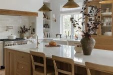a cozy modern earthy kitchen with neutral lower cabinets, a large stained kitchen island, a large cupboard, a built-in hood and pendant lamps