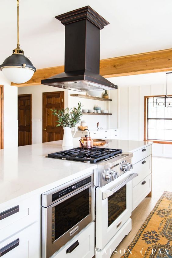 a cozy white farmhouse space with a cooker and a black hood, a pendant lamp and a boho rug