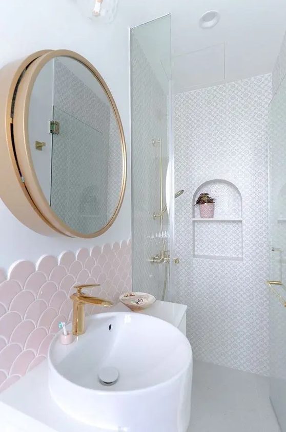 a cute bathroom done with blush fihscale and neutral printed tiles, a sink, a mirror cabinet in a gold frame is chic and cool
