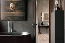 a delicate Gothic bathroom in black, with concrete walls, a stone tub, a rough wooden stool and a beautiful vintage artwork