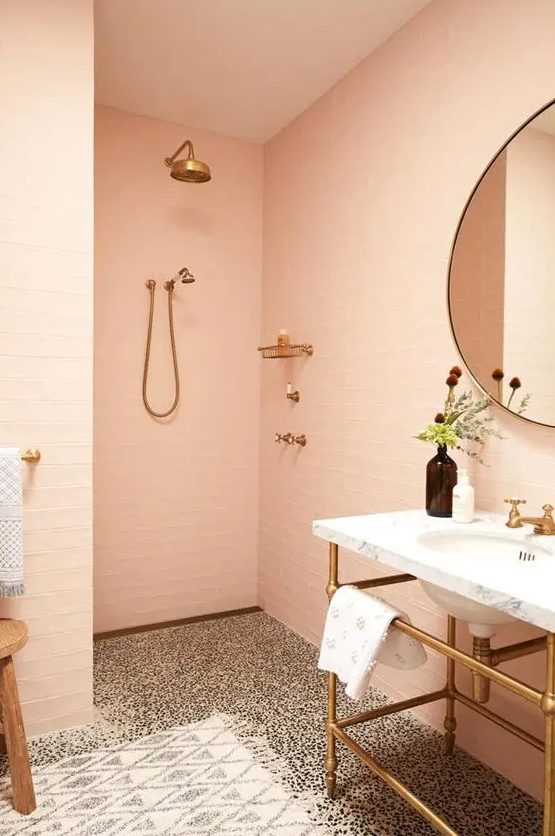 A delicate peachy pink bathroom clad with tiles, a terrazzo floor, a free standing sink and a round mirror is very soft