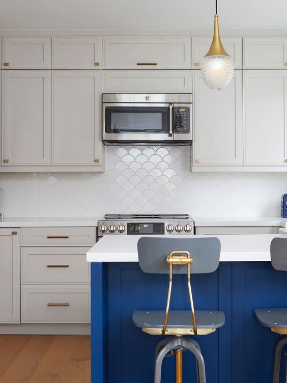 a dove grey kitchen with shaker cabinets, a bold blue kitchen island, white countertops, a white scallop tile backsplash and lamps