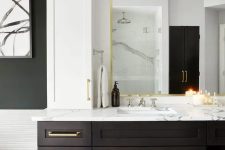 a dramatic bathroom with a large dark-stained vanity with a mirror in a gilded frame, a white stone countertop and gold touches