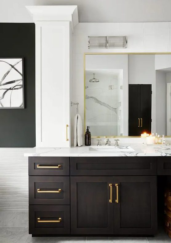 A dramatic bathroom with a large dark stained vanity with a mirror in a gilded frame, a white stone countertop and gold touches