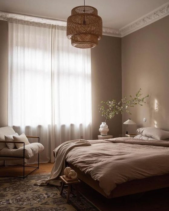 a dreamy light brown bedroom with a bed with neutral bedding, a printed rug, a woven pendant lamp and a white chair