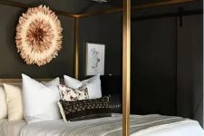 a glam moody bedroom with soot walls and a ceiling, a gold canopy bed with neutral bedding, a woven bench and a crystal chandelier