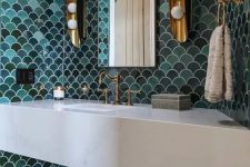 a gorgeous sink space with green and aqua fishscale tiles, a stone vanity, vintage brass fixtures and wall sconces