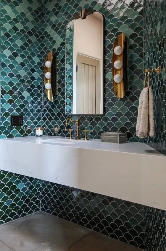 a gorgeous sink space with green and aqua fishscale tiles, a stone vanity, vintage brass fixtures and wall sconces