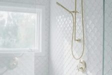 a gorgeous white bathroom clad with fishscale tiles, a shower space with a window, gold fixtures is elegant and cool
