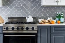 a grey and white kitchen with white countertops and a grey fish scale tile backsplash plus stainless steel appliances