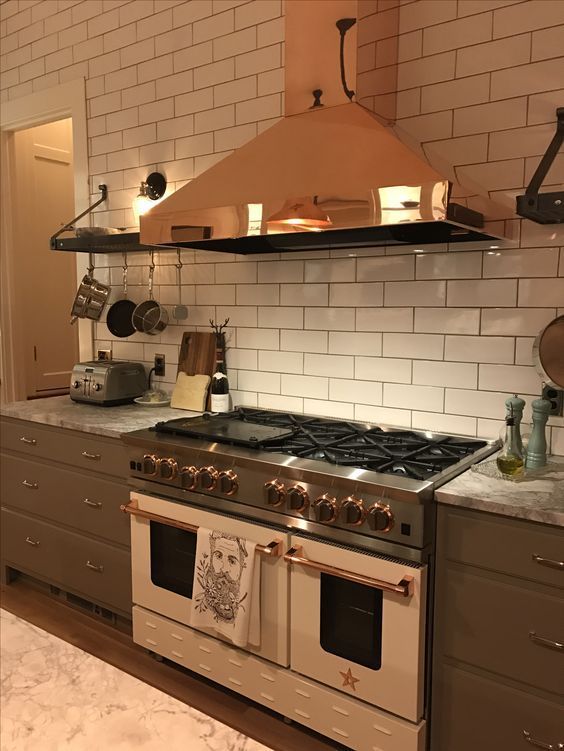a grey kitchen with grey countertops, a white subway tile backsplash and a gold hood over the cooker