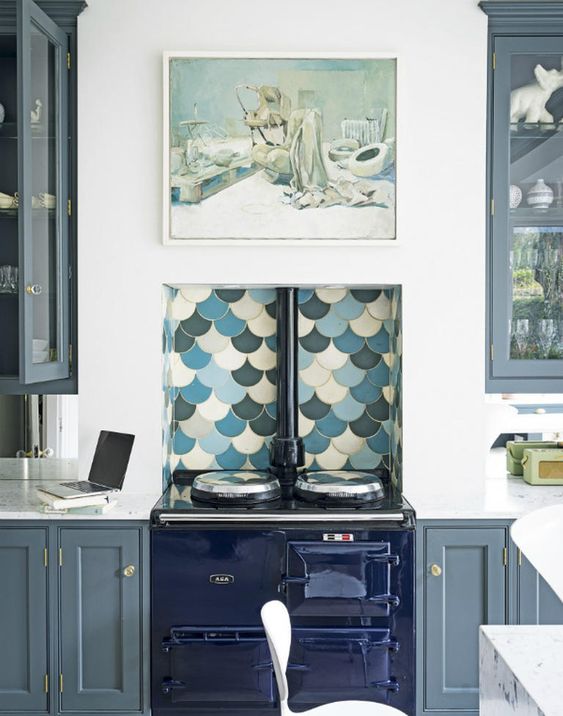 a grey kitchen with shaker cabinets, a glossy navy cooker, a bright fish scale backsplash and a painting