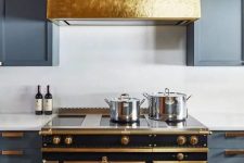 a grey kitchen with shaker cabinets, white stone countertops and a backsplash, a shiny gold hood over a chic vintage cooker
