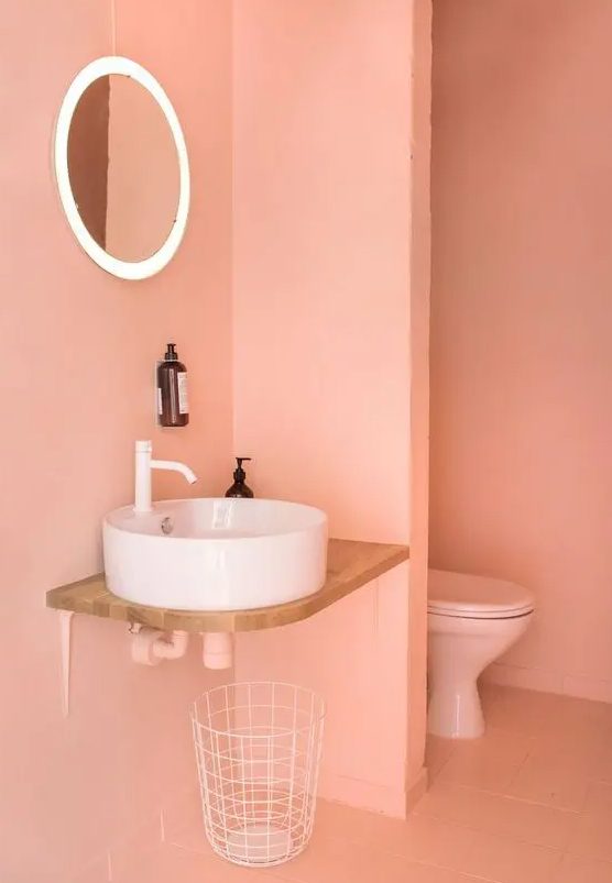 A jaw dropping Peach Fuzz bathroom with a vessel sink, a lit up mirror, white appliances and everything minimal