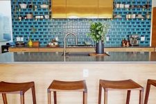 a jaw-dropping kitchen with tan cabinets, a large polished gold hood, a bold blue backsplash and a matching floor