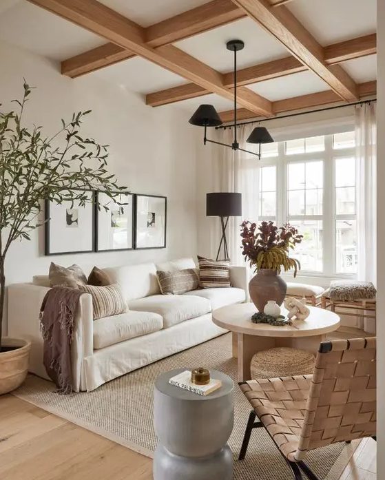 a light-filled earthy living room with wooden beams, a white sofa, stools and a woven chair, a grey side table and a round coffee table