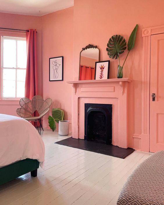 a lively Peach Fuzz bedroom with a fireplace, a bed, a rattan chair, some potted plants and decor