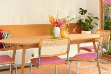 a lively dining room with a buil-in bench, a table, pink chairs with cane backs, a Peach Fuzz rug and some plants