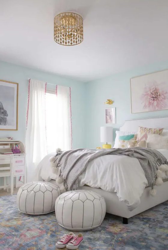 a lively teen girl bedroom with aqua walls, a white bed with printed pillows, white poufs, a white desk and a chair, a gold chandelier