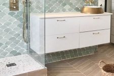 a lovely and welcoming bathroom done with pale green fish scale tiles, a white vanity, a sink, a mirror and a basket
