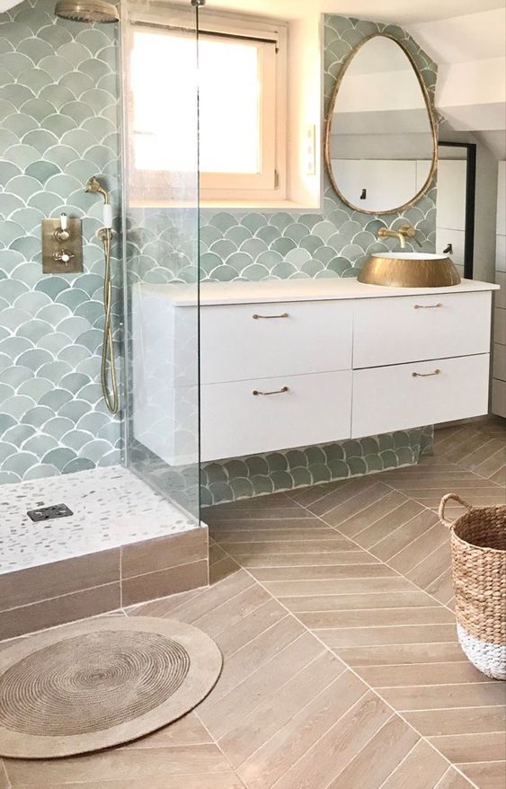 a lovely and welcoming bathroom done with pale green fish scale tiles, a white vanity, a sink, a mirror and a basket