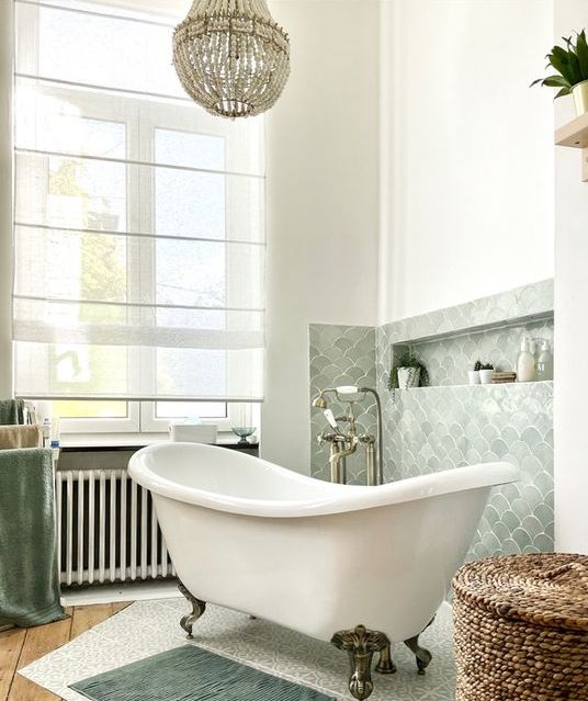 a lovely bathroom with a pale green fish scale backsplash, a free-standing tub, a basket and some rugs