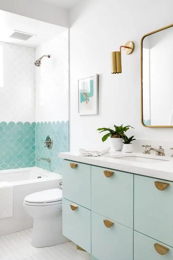 a lovely beach bathroom with mint green touches, fish scale tiles in the shower and a mint floating vanity and brass touches
