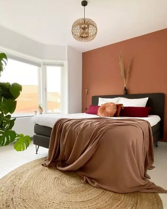 a lovely bedroom with a boho feel, a terracotta accent wall, a black bed, bold bedding, a wooden pendant lamp and some plants