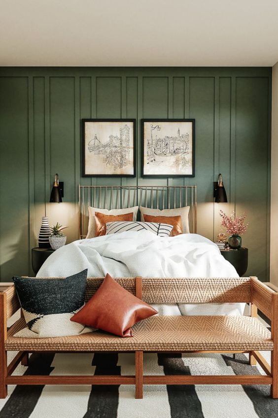 a lovely boho meets modern earthy bedroom with grene paneling, a bed with neutral bedding, a bench with pillows and sconces