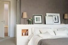 a lovely modern bedroom with a taupe accent wall, a white bed with a storage headboard, artworks and lamps and white bedding
