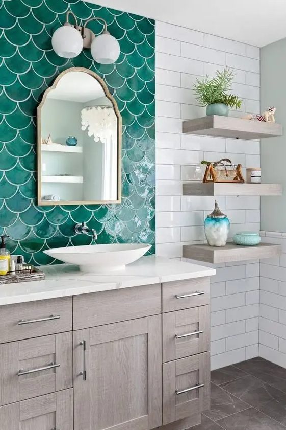 a lovely seaside bathroom done with white subway and emerald fishscale tiles, a stained vanity and open shelves, a wall lamp