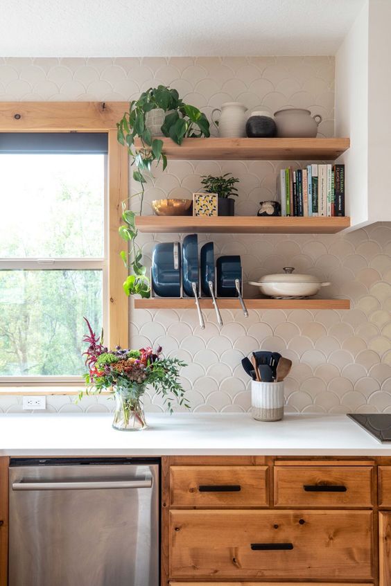 a lovely stained kitchen with white cabinets, open shelves, a white fish scale tile backsplash, greenery and blooms