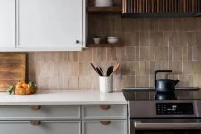 a lovely two-tone kitchen with white countertops, a beige tile backsplash, a fluted hood and a cooker